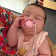 Giulia participe au concours pour gagner de l'argent avec cette photo : baby, pacifier, sleeping, infant, person, hand, arm, clothing, floral, fabric, indoor, child, blurred_background, holding, cute, peaceful, skin, pink, soft_lighting, portrait