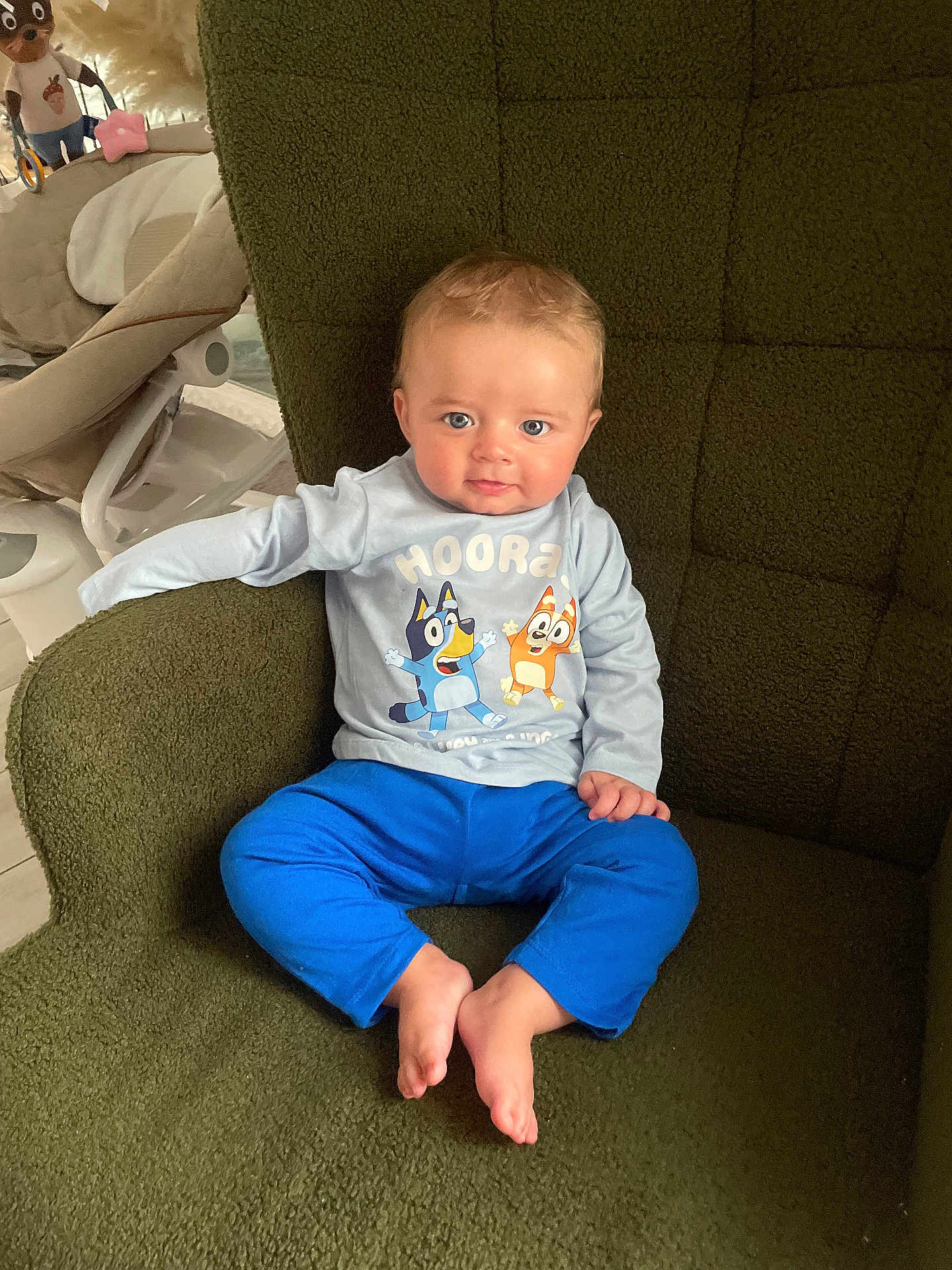 Kiezyo participe au concours pour gagner de l'argent avec cette photo : baby, child, blue_eyes, cartoon_shirt, blue_pants, green_chair, indoor, cute, sitting, barefoot, smiling, curious, young_child, soft_lighting, home_interior, comfortable, portrait, toddler, innocent, cozy