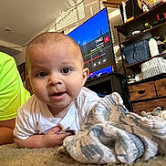 Wesley is registered to the contest to win money with this photo: baby, child, indoor, carpet, blanket, person, face, eyes, smile, television, furniture, shelf, drawer, clothing, living_room, curious, home, young_child, candid, casual