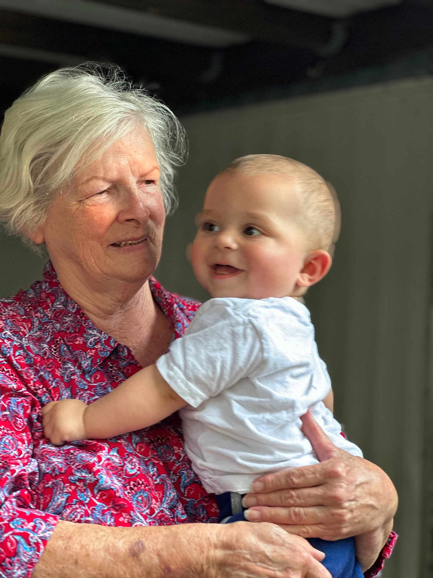 Wesley joined the competition — help win amazing prizes! baby, child, elderly_woman, person, smiling, holding, affection, indoor, portrait, white_hair, red_shirt, patterned_clothing, happy, closeup, skin, face, hands, casual_clothing, background_blur, family