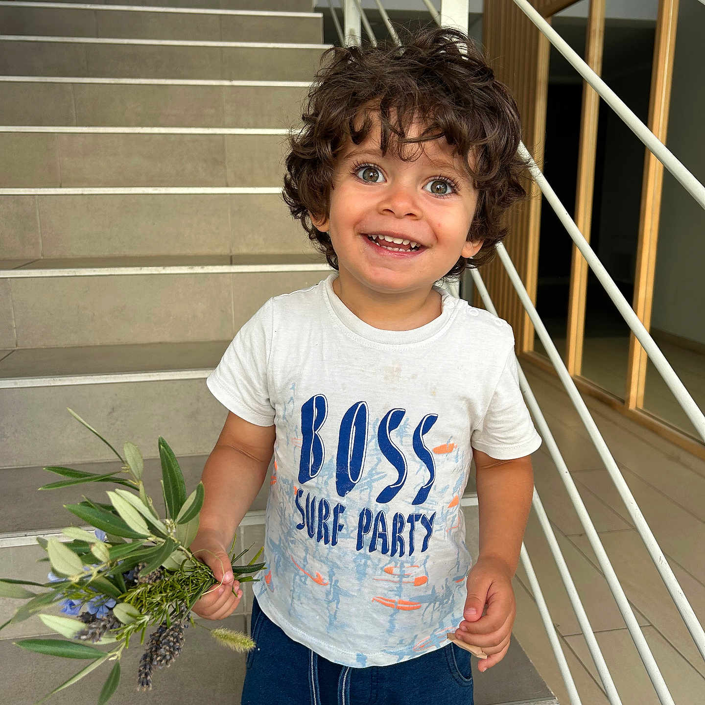 Nael participe au concours pour gagner de l'argent avec cette photo : bouquet, casual_clothing, child, curly_hair, cute, eyes, flowers, hair, happy, holding, indoor, person, portrait, railing, shorts, smiling, staircase, standing, toddler, tshirt