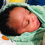 Nqaba joined the competition — help win amazing prizes! baby, infant, face, hoodie, green_clothing, curly_hair, bed, blanket, pillow, soft_texture, indoor, child, newborn, cute, sleepwear, closeup, portrait, resting, comfort, baby_bottle