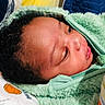 baby, infant, face, hoodie, green_clothing, curly_hair, bed, blanket, pillow, soft_texture, indoor, child, newborn, cute, sleepwear, closeup, portrait, resting, comfort, baby_bottle