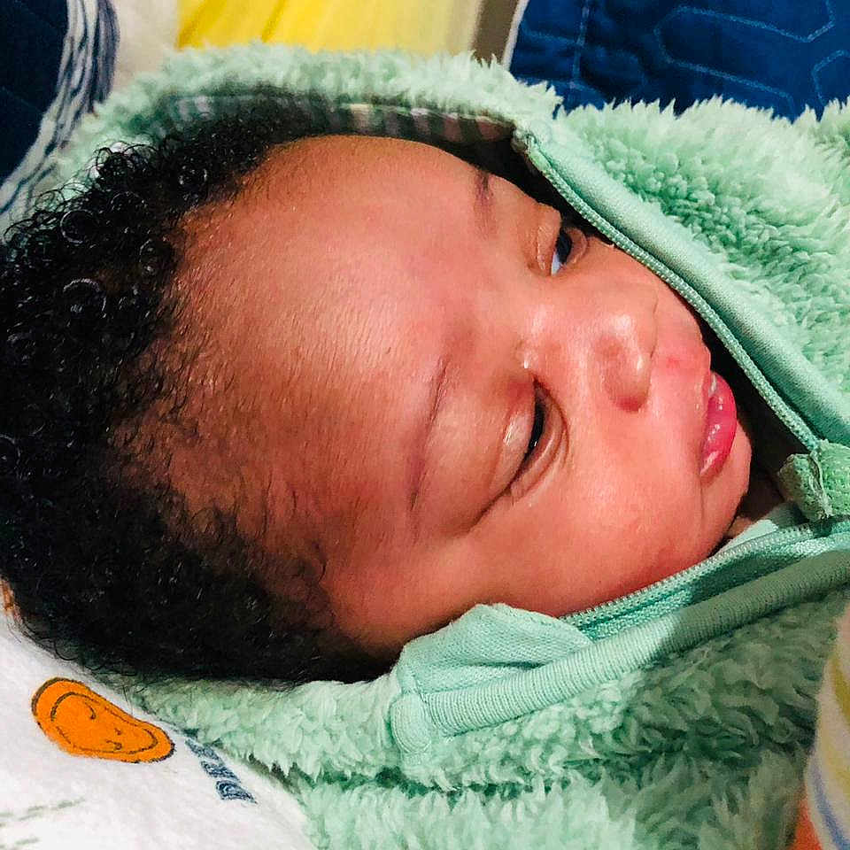 Nqaba joined the competition — help win amazing prizes! baby, infant, face, hoodie, green_clothing, curly_hair, bed, blanket, pillow, soft_texture, indoor, child, newborn, cute, sleepwear, closeup, portrait, resting, comfort, baby_bottle
