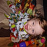 toddler, child, pajamas, curly_hair, smiling, toy, blanket, indoor, playpen, colorful, cute, happy, face, person, infant, plush_toy, patterned_clothing, baby, lying_down, bright