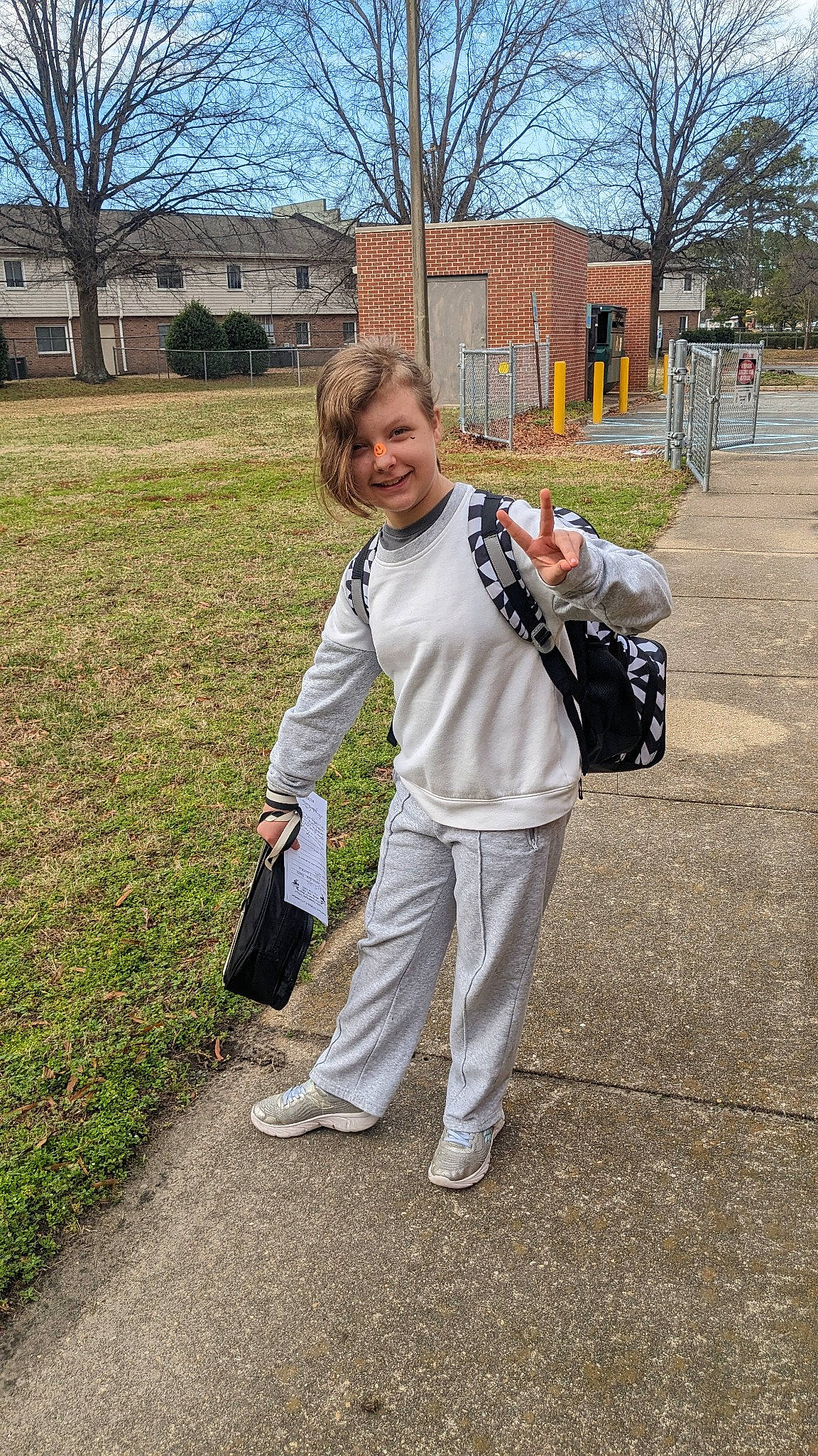 Samantha is registered to the contest to win money with this photo: backpack, bag, blond, child, denim, fun, gesture, grass, handbag, joy, leisure, luggage_and_bags, person, plant, recreation, sidewalk, sky, sweatpant, t_shirt, tree