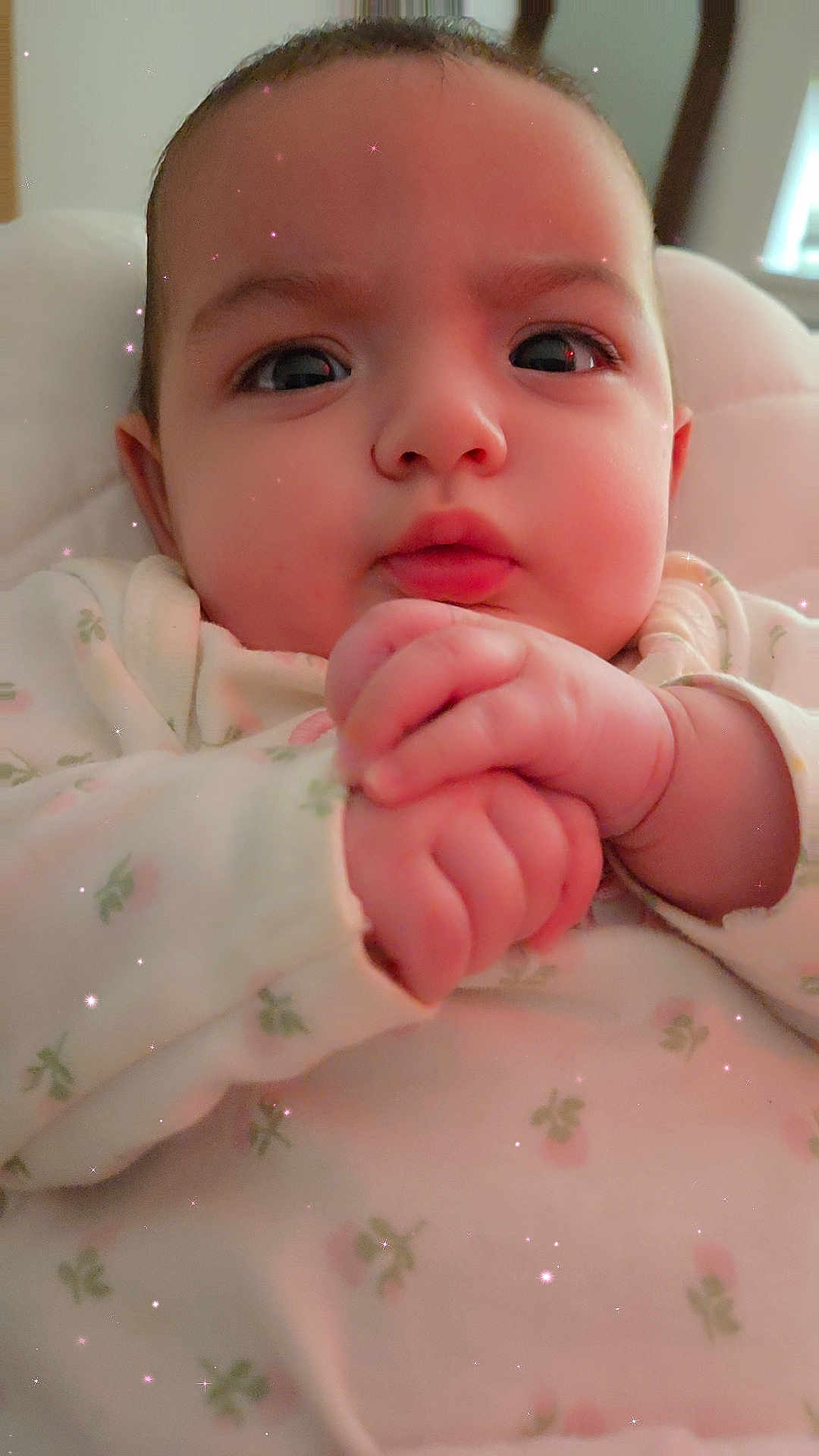 Ansley is registered to the contest to win money with this photo: baby, infant, close_up, hands, face, eyes, onesie, floral_pattern, cute, chubby_cheeks, soft_lighting, indoors, portrait, child, adorable, sparkles, skin, expression, young, newborn