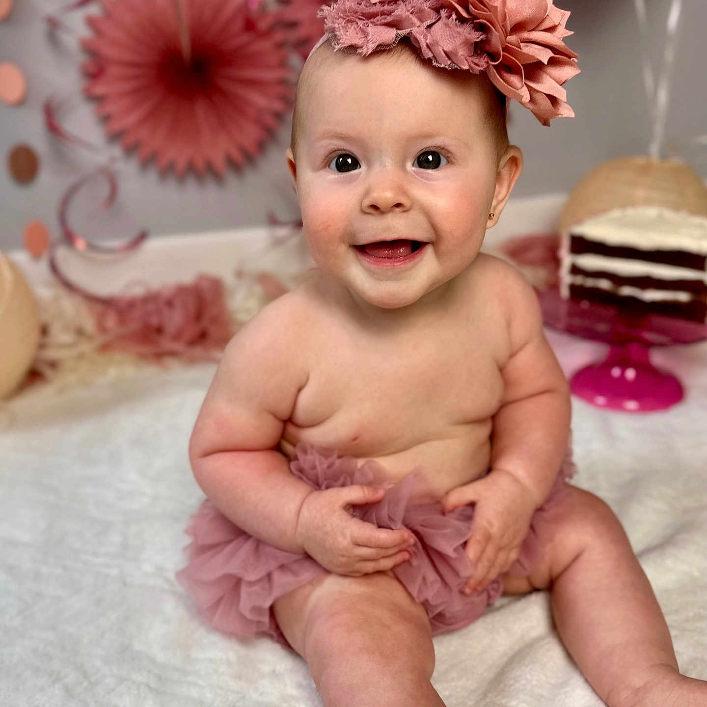 Raleigh is registered to the contest to win money with this photo: baby, smiling, tutu, headband, flower, pink, cake, birthday, celebration, decorations, happy, cute, sitting, indoors, child, face, portrait, festive, person, fun