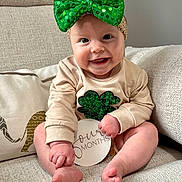 Raleigh is registered to the contest to win money with this photo: baby, infant, smiling, green_bow, sequin, four_months, couch, beige, clothing, cute, headband, shamrock, holding, sitting, happy, indoors, portrait, child, person, feet