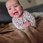 Emy participe au concours pour gagner de l'argent avec cette photo : baby, smiling, blue_eyes, rosy_cheeks, blanket, hand, clothing, floral_pattern, face, expression, young_child, indoor, soft_texture, portrait, cute, happy, lying_down, infant, skin, closeup