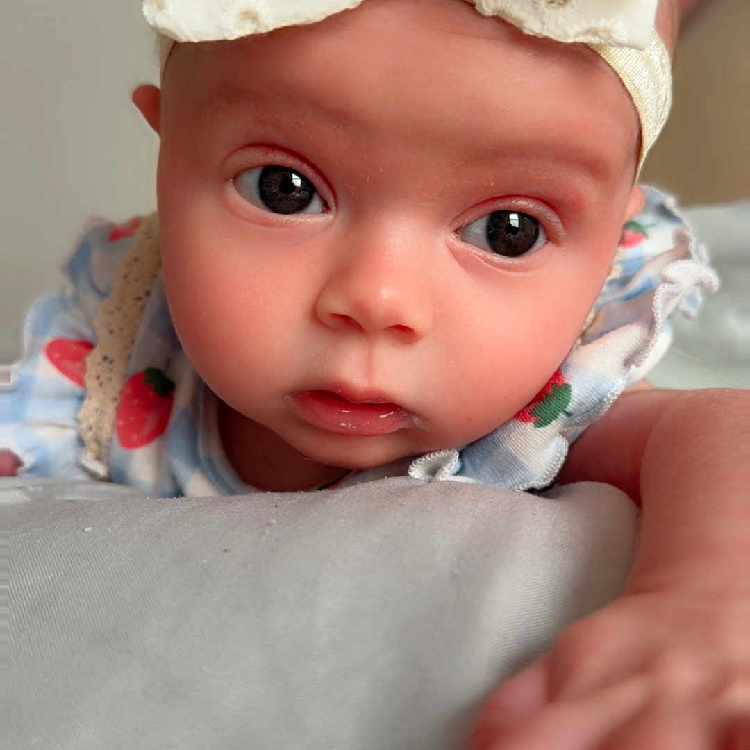 Elianna joined the competition — help win amazing prizes! baby, infant, headband, bow, face, hand, curious, cute, expression, closeup, portrait, skin, eyes, clothing, pattern, soft_lighting, indoor, child, young, cute_outfit