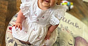 Delilah is registered to the contest to win money with this photo: baby, child, cute, smiling, red_hair, white_dress, indoor, floor, rug, elephant, toy, playful, curly_hair, happy, sitting, portrait, wooden_floor, home, infant, adorable
