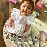 baby, child, cute, smiling, red_hair, white_dress, indoor, floor, rug, elephant, toy, playful, curly_hair, happy, sitting, portrait, wooden_floor, home, infant, adorable
