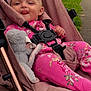 baby, child, stroller, pink_clothing, plush_toy, outdoor, park, tongue_out, happy, seatbelt, infant, grass, pathway, cute, person, smiling, nature, relaxed, casual, baby_girl