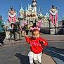 toddler, child, castle, disneyland, red_sweater, minnie_mouse, white_skirt, pink_bows, boots, outdoor, daylight, people, tourists, blue_sky, holiday_decorations, walking, shadow, fun, theme_park, smiling