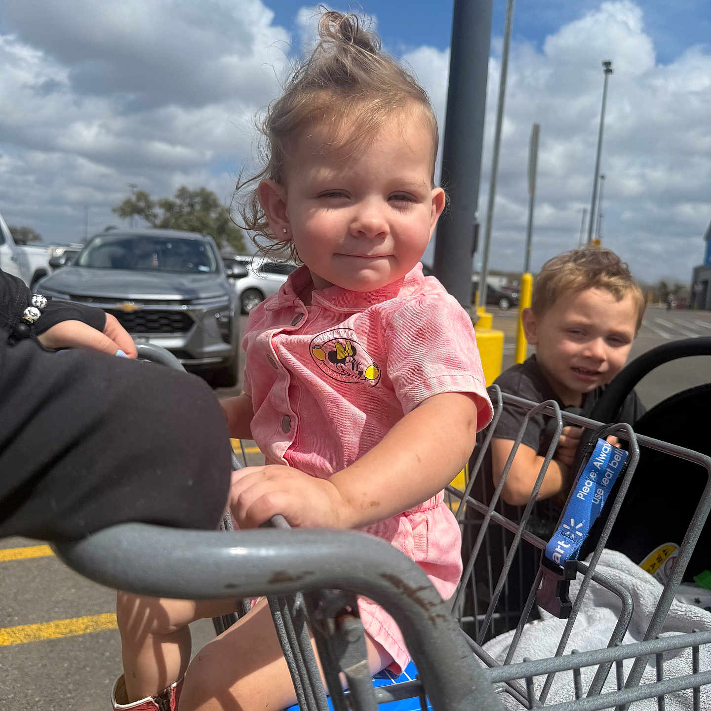 Emberlynn is registered to the contest to win money with this photo: child, toddler, shopping_cart, outdoor, parking_lot, sky, clouds, car, boy, girl, clothing, person, daylight, footwear, metal, hand, expression, urban, casual, family