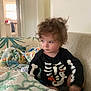 Grayson joined the competition — help win amazing prizes! toddler, child, curly_hair, skeleton_shirt, couch, blanket, baby_bottle, indoors, window, door, wall_art, furniture, clothing, portrait, seated, looking_away, cozy, home, soft_lighting, expression