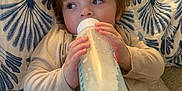 Grayson joined the competition — help win amazing prizes! child, toddler, milk_bottle, curly_hair, couch, cushion, beige_clothing, indoor, baby, feeding, relaxed, patterned_pillow, milk, hand, face, portrait, cozy, infant, young_child, casual