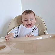 Victor participe au concours pour gagner de l'argent avec cette photo : baby, bib, child, clothing, cute, expression, face, furniture, hands, happy, high_chair, indoor, infant, light, person, reflection, seat, sitting, smiling, young_child