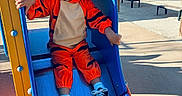 Warren participe au concours pour gagner de l'argent avec cette photo : child, toddler, curly_hair, orange_costume, tiger_costume, slide, playground, outdoor, sunny_day, shoes, socks, curious, playing, blue_slide, yellow_structure, bench, shadow, casual_clothing, fun, recreation