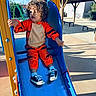 child, toddler, curly_hair, orange_costume, tiger_costume, slide, playground, outdoor, sunny_day, shoes, socks, curious, playing, blue_slide, yellow_structure, bench, shadow, casual_clothing, fun, recreation