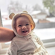 Chase joined the competition — help win amazing prizes! baby, smiling, onesie, bear_ears, window, snow, arm, indoor, child, cute, happy, portrait, soft_texture, warm_clothing, face, person, infant, cozy, background_blur, holding