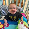Chase is registered to the contest to win money with this photo: baby, crib, smile, nirvana_tshirt, cushion, colorful, child, indoor, happy, face, hand, pillow, blanket, furniture, person, infant, home, cute, playful, soft