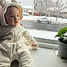 Chase is registered to the contest to win money with this photo: baby, child, infant, onesie, white_clothing, window, snow, winter, plant, potted_plant, green_plant, indoor, cozy, cute, face, portrait, sitting, curious, home, daylight