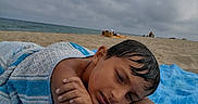 Soran participe au concours pour gagner de l'argent avec cette photo : child, beach, towel, blue, sand, sea, cloudy_sky, relaxed, lying_down, portrait, outdoor, person, vacation, summer, water, calm, nature, travel, resting, holiday