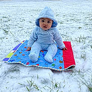Elias De Luna joined the competition — help win amazing prizes! baby, child, snow, outdoor, blanket, blue_clothing, hood, grass, house, winter, cold, sitting, curious, person, yard, nature, daylight, cute, infant, playtime