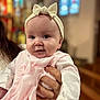 baby, infant, face, headband, bow, pink_clothing, hand, person, portrait, indoors, blurred_background, stained_glass, church, cute, soft_light, child, holding, closeup, warm, smiling
