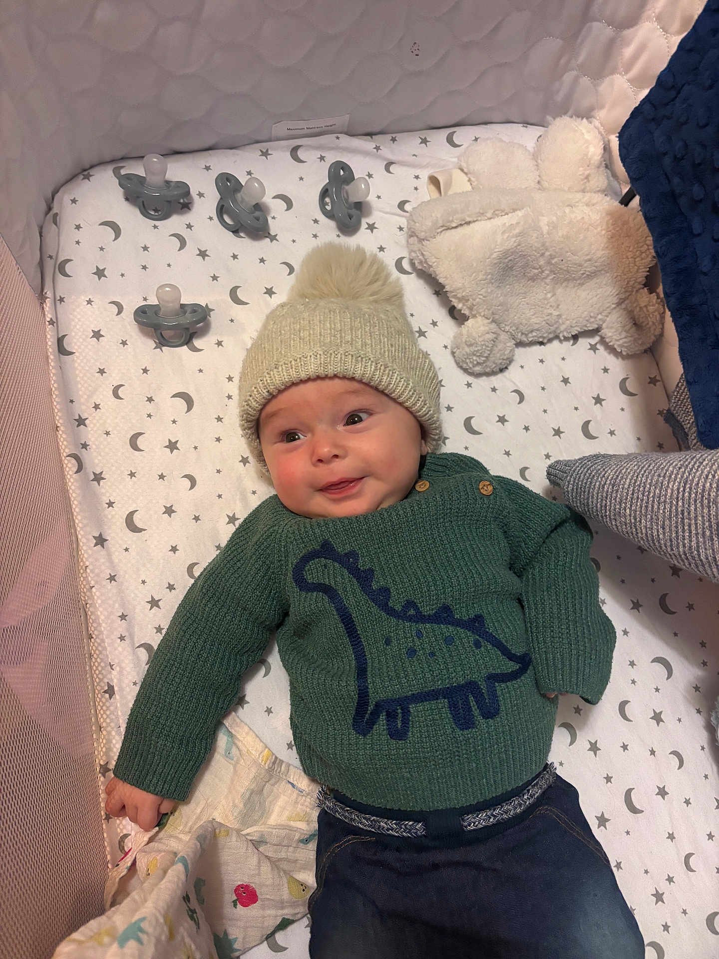 Austin joined the competition — help win amazing prizes! baby, infant, hat, knitted_hat, pom_pom, green_sweater, dinosaur_design, crib, pacifier, teddy_bear, plush_toy, diaper, blanket, moon_pattern, star_pattern, sleeping_area, child, cute, smiling, cozy