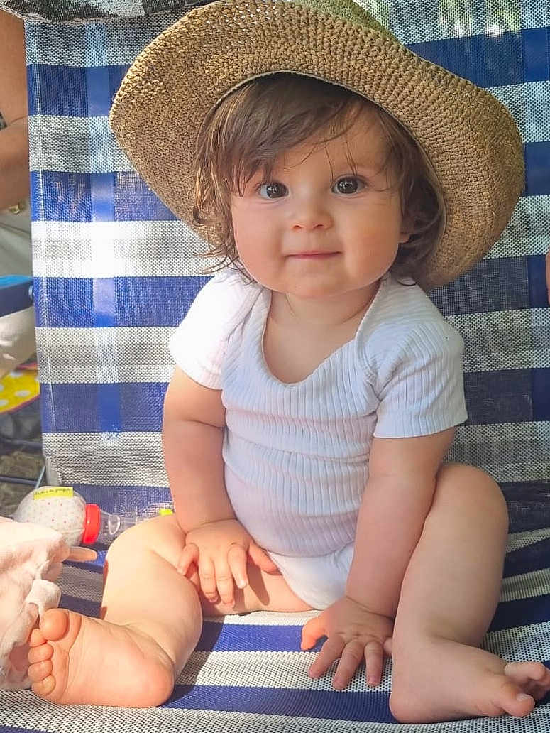 Aria a rejoint le concours — aidez-le/la à gagner de superbes lots ! baby, child, hat, onesie, striped_chair, outdoor, smiling, cute, barefoot, toddler, sunlight, portrait, sitting, happy, skin, hand, foot, face, hair, person