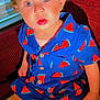 Ayla is registered to the contest to win money with this photo: toddler, child, blue_clothing, watermelon_pattern, curly_hair, earrings, indoor, couch, red_couch, portrait, sitting, bright_colors, expression, face, eyes, hand, buttoned_shirt, shorts, casual, young_child