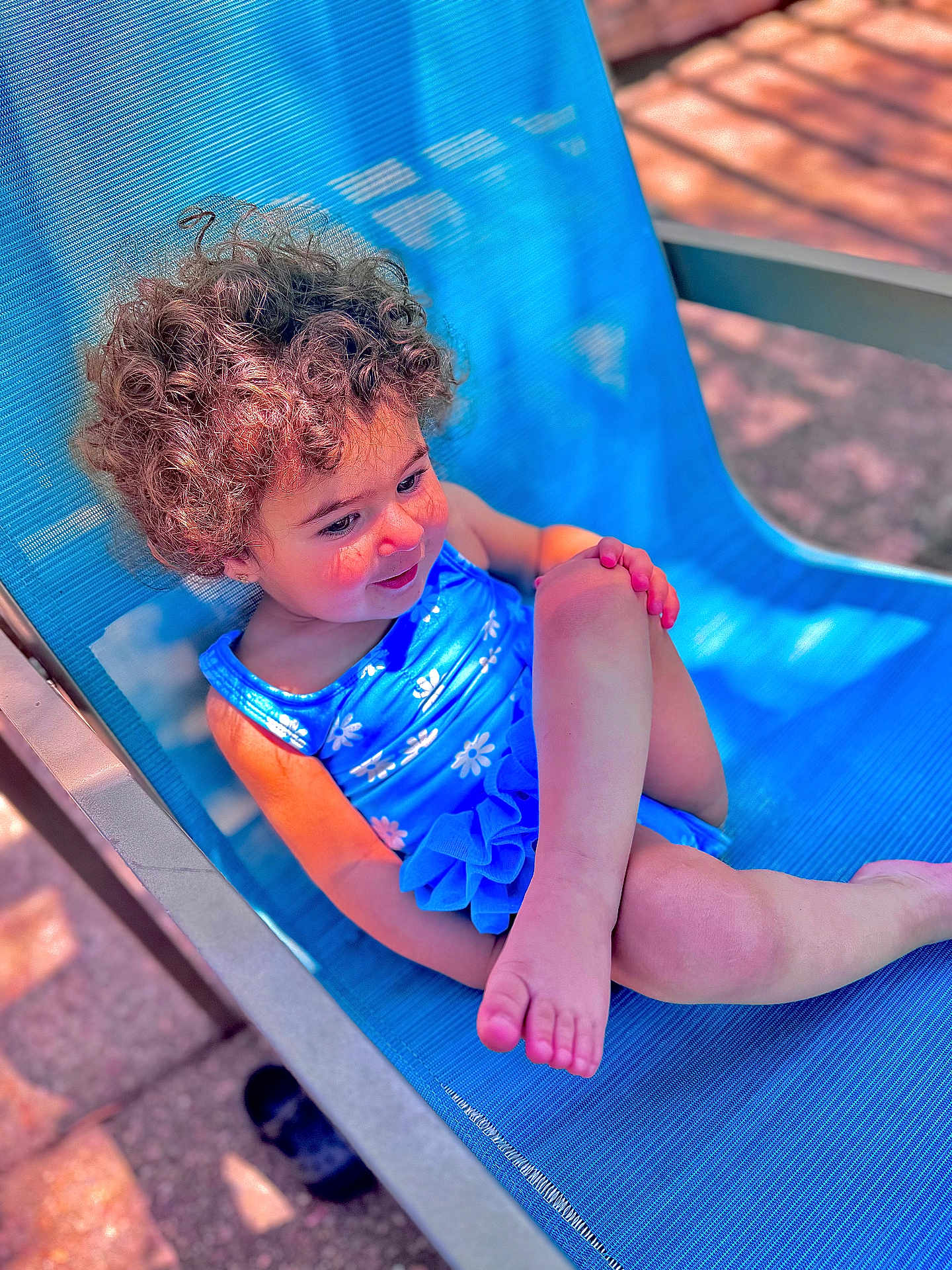 Ayla is registered to the contest to win money with this photo: child, toddler, curly_hair, blue_swimsuit, outdoor_chair, sunlight, relaxed, smiling, barefoot, summer, playful, skin, person, seat, leisure, daylight, happy, resting, blue, texture