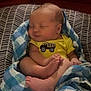 baby, infant, sleeping, blanket, yellow_clothing, onesie, dump_truck, patterned_cushion, blue, checkered, feet, toes, face, peaceful, indoor, soft_lighting, red_background, cute, child, resting