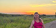 Zoe is registered to the contest to win money with this photo: casual_clothing, dog, dreadlocks, evening, field, grass, happy, leash, nature, outdoor, pet, road, rural, skirt, smiling, sunset, tank_top, tattoos, walking, woman