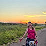 casual_clothing, dog, dreadlocks, evening, field, grass, happy, leash, nature, outdoor, pet, road, rural, skirt, smiling, sunset, tank_top, tattoos, walking, woman