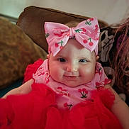 Scarlett-Ann joined the competition — help win amazing prizes! baby, background_blur, bow, cherry_pattern, child, closeup, clothing, couch, cute, face, happy, headband, indoor, infant, person, portrait, red_dress, sitting, smile, soft_lighting