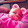 baby, pacifier, pink_clothing, digital_filter, bear_ears, heart_ears, indoor, closeup, child, resting, soft_texture, adult_arm, face, cute, portrait, cozy, smiling, pink_tone, furniture, blanket