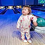 child, toddler, bowling_alley, bowling_lane, bowling_ball, wooden_floor, sneakers, motion_blur, bowling_pins, indoor, recreation, family_activity, hoodie, patterned_clothing, lanes, screen, ambient_lighting, fun, playful, spectator_area