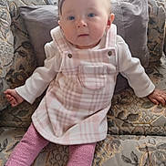 Azzalia is registered to the contest to win money with this photo: baby, child, clothing, couch, cozy, cushion, cute, expression, face, home, indoor, infant, patterned_fabric, person, pink_leggings, plaid_dress, portrait, sitting, soft_lighting, young_child