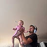 Raeah is registered to the contest to win money with this photo: baby, child, man, headphones, indoor, smile, happy, lifting, pink_dress, ceiling, room, joy, person, holding, clothing, light, home, fun, family, playful