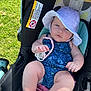 baby, child, stroller, hat, pacifier, outdoor, grass, sunlight, summer, blue_outfit, skin, legs, hand, face, expression, infant, clothing, accessory, seat, warning_label