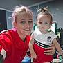 woman, child, toddler, smile, red_clothing, indoor, person, hair, face, holding, casual, room, furniture, television, blue_wall, expression, portrait, family, home, people