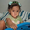 child, toddler, girl, portrait, smiling, serious_expression, indoors, bedroom, bed, pillow, striped_bedding, green_shirt, hair_bows, hair_accessories, play_toy, steering_wheel, sitting, curly_hair, face, furniture