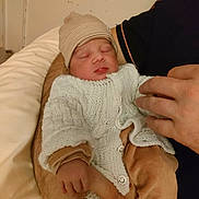 Hugo participe au concours pour gagner de l'argent avec cette photo : baby, newborn, sleeping, knitted_clothes, hat, hand, adult, arms, comfort, cozy, indoor, person, skin, fingers, sleep, warm, gentle, infant, closeup, rest