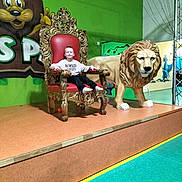 Nathan a rejoint le concours — aidez-le/la à gagner de superbes lots ! child, boy, throne, chair, lion_statue, indoor, play_area, green_wall, mural, smiling, casual_clothing, socks, platform, decorative_chair, artificial_lion, playful, young_person, portrait, seated, happy
