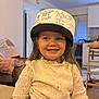Esmée participe au concours pour gagner de l'argent avec cette photo : child, girl, smiling, helmet, handwritten_text, sweater, indoor, living_room, furniture, wooden_chair, table, cozy, happy, portrait, casual_clothing, long_hair, cute, playful, home, young