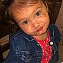 child, girl, pigtails, denim_jacket, red_shirt, indoor, table, chair, playful, cute, face, portrait, expression, brown_eyes, hair_ties, casual_clothing, smirk, seated, tile_floor, furniture
